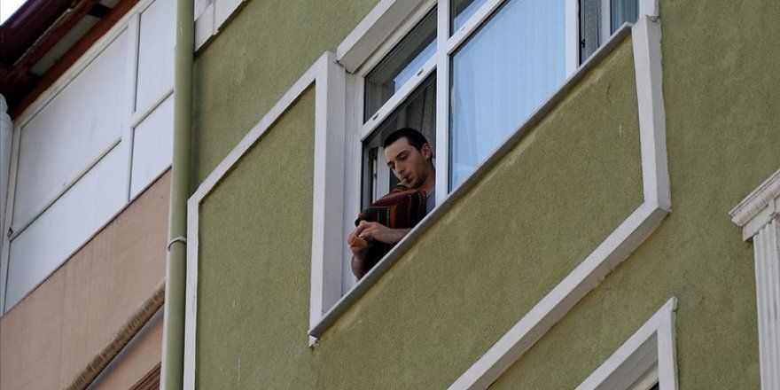 Evinin penceresinden çaldığı tulumla komşularına moral veriyor